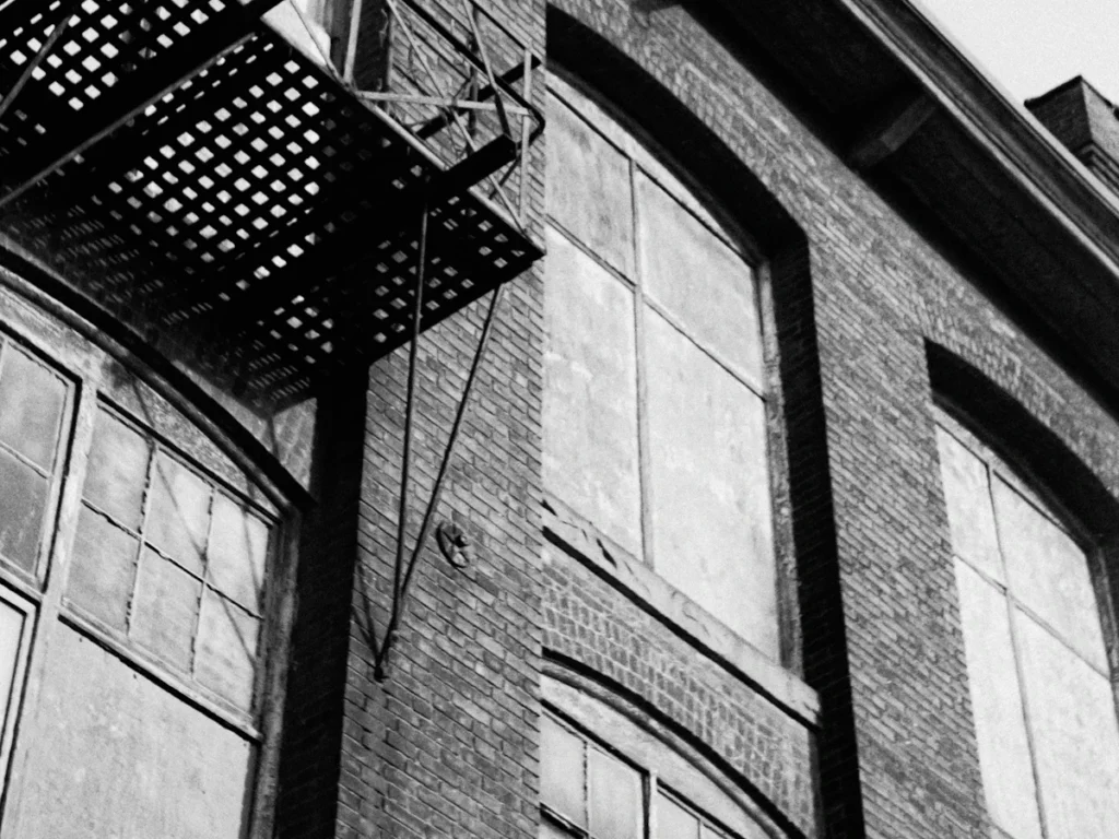 Fire escape platform with grating and a ladder on a brick building, the ladder and stair operation checked during testing in Westchester