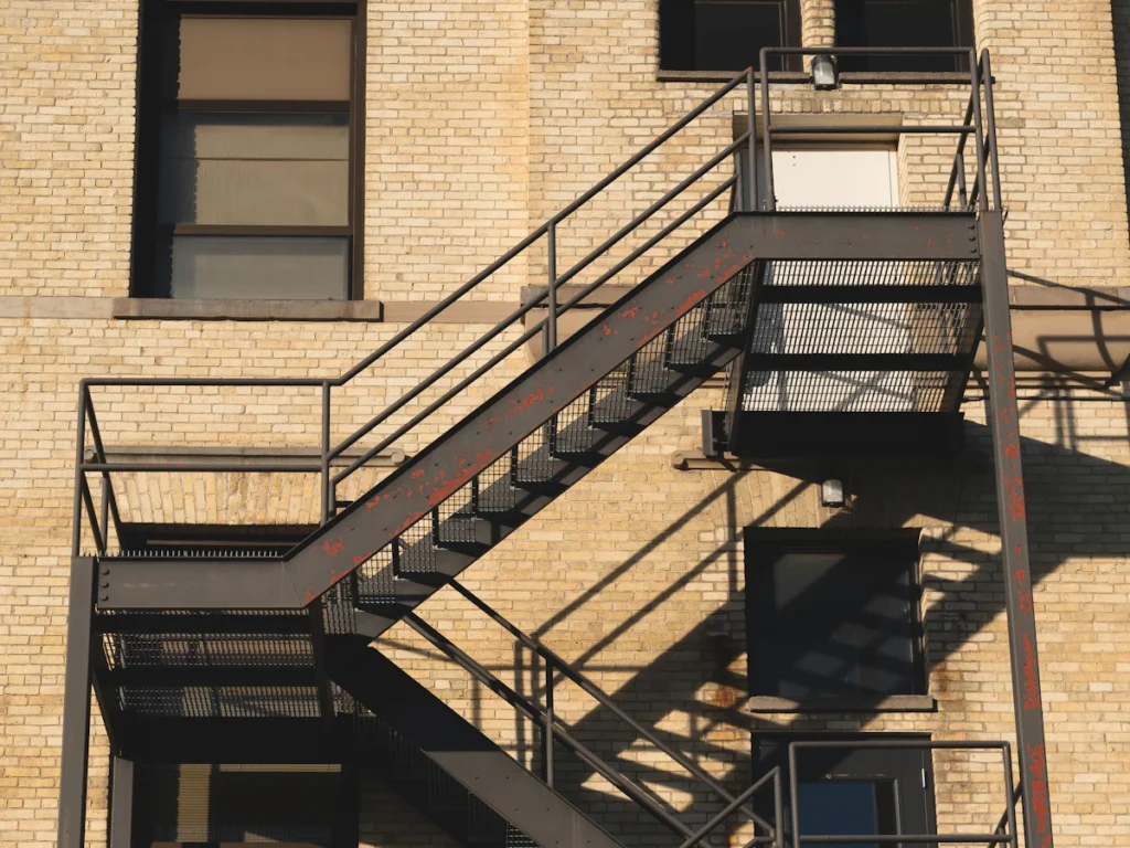 Steel fire escape stairs and landings outside apartment windows on a brick building, repaired while tenants stay in place in Westchester