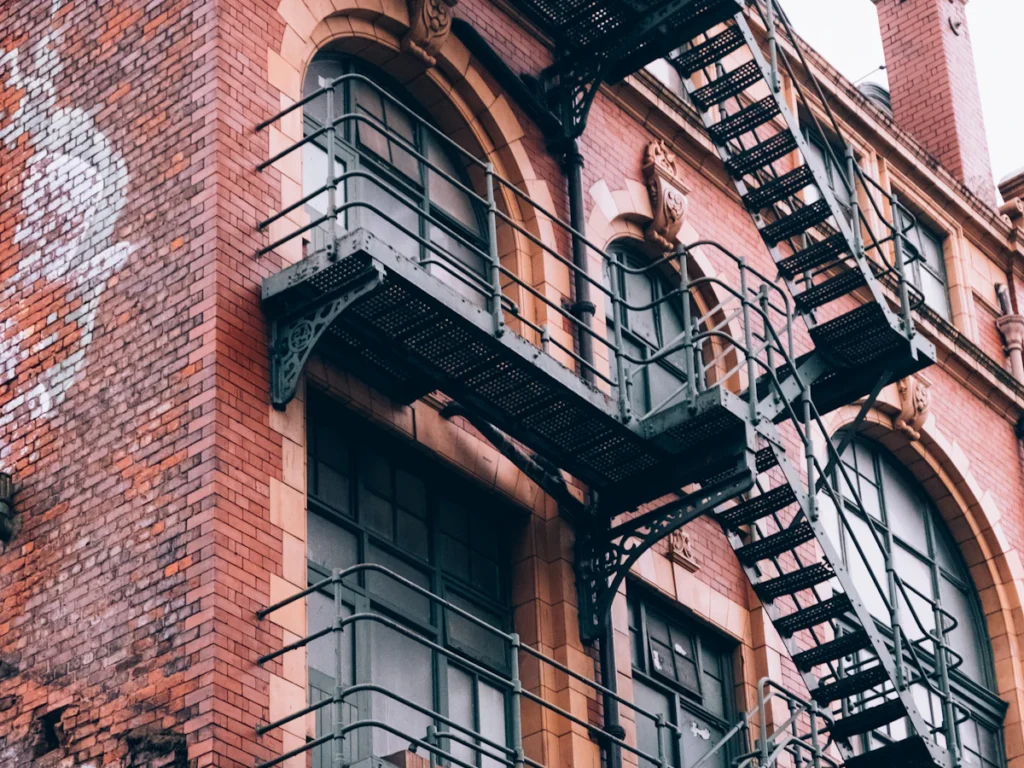 Black steel fire escape balconies and stairs on an old red brick building, the kind of structure replaced with new steel in Westchester NY